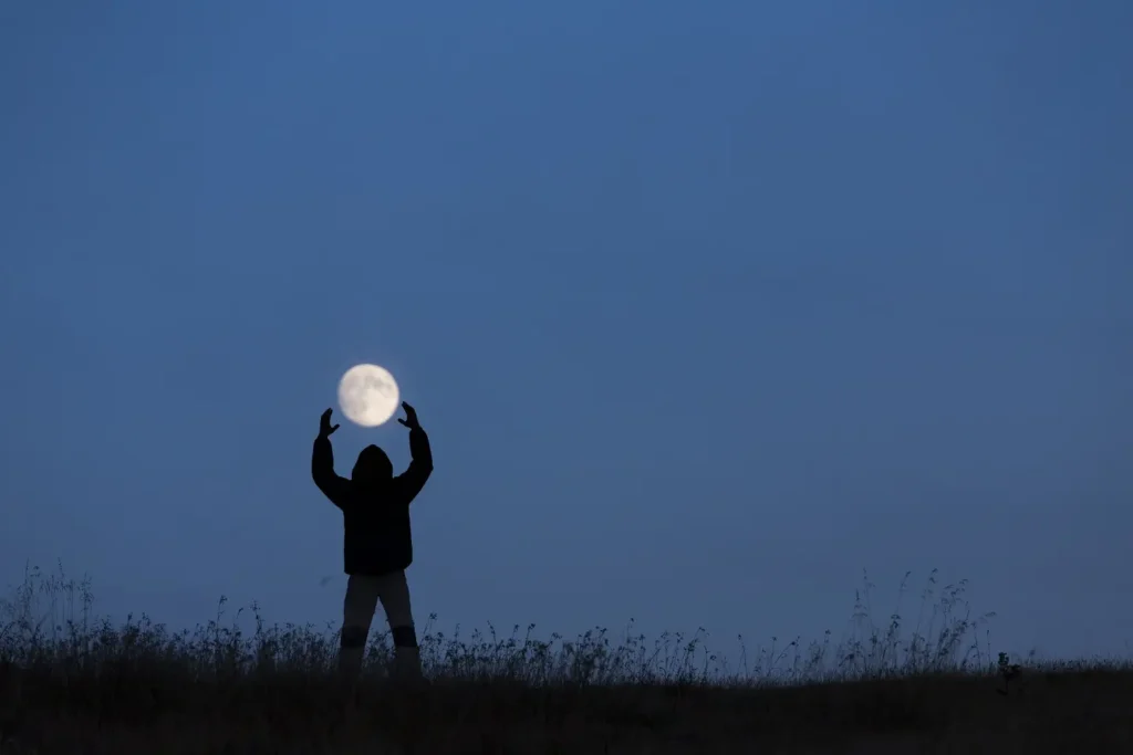 silhouette tendant vers la lune dans un cadre naturel